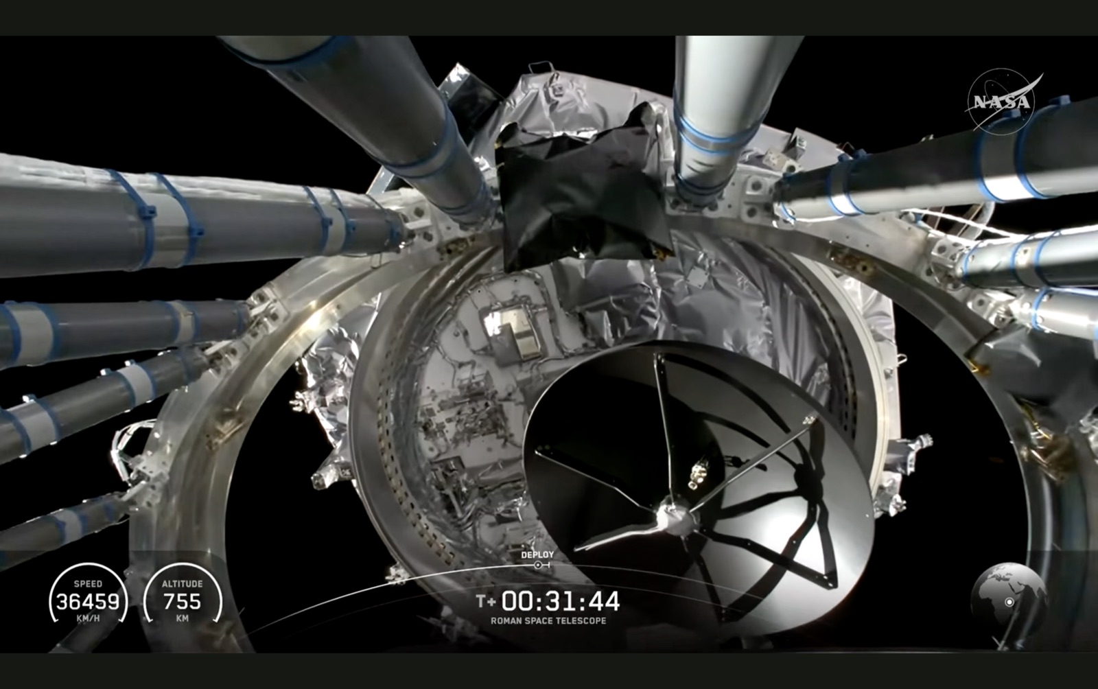 Looking down into the top of the Falcon Heavy second stage against the black of space. A ring of silver struts and blue-banded tubes splays outward around a circular bay lined with crumpled insulation foil, with a dark finned structure at its centre. Telemetry reads T+00:31:44, deploy, speed 36,459 km/h, altitude 755 km.